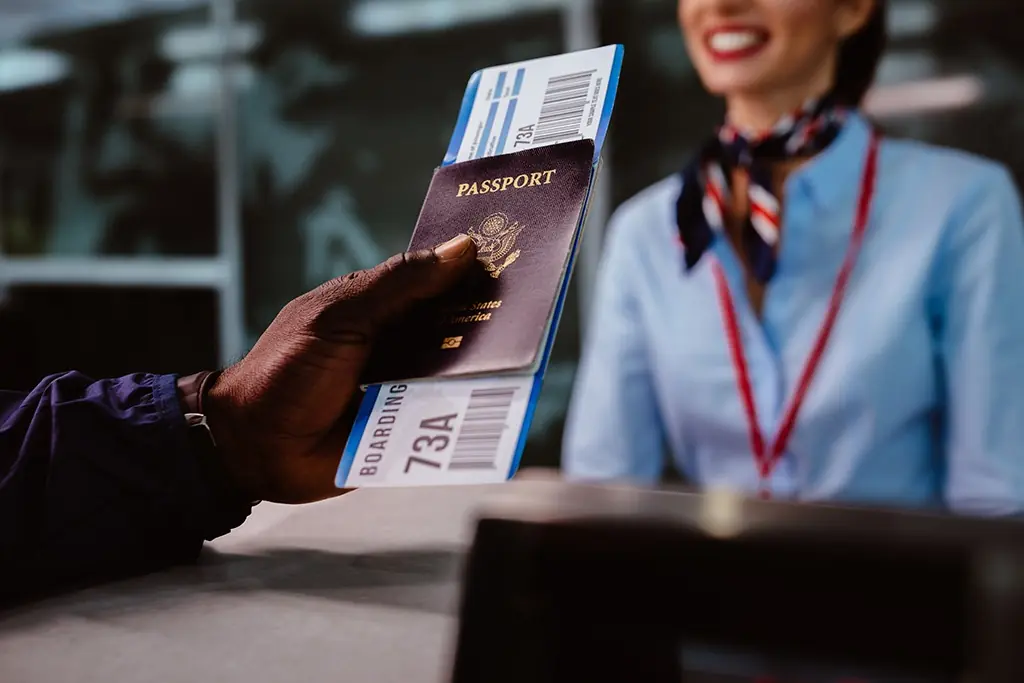 A man's hand passes a passport and boarding pass to a woman in a flight attendant uniform