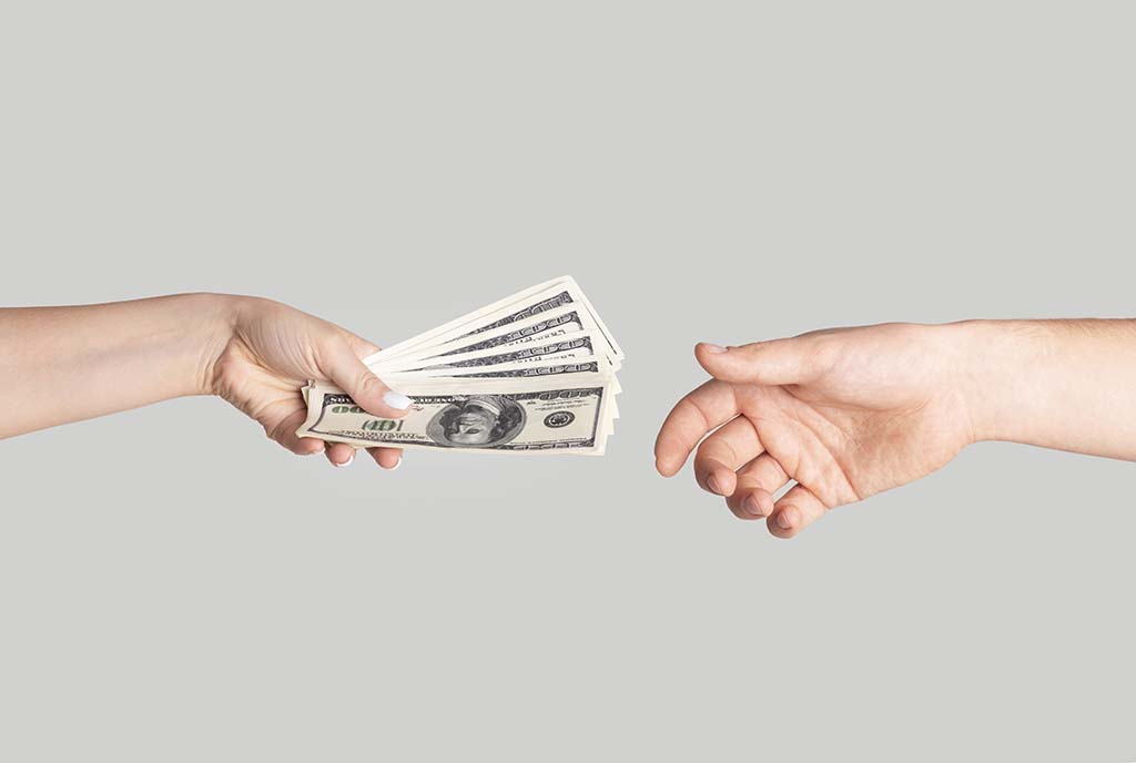 A hand holding money reaches out to another hand, which is empty