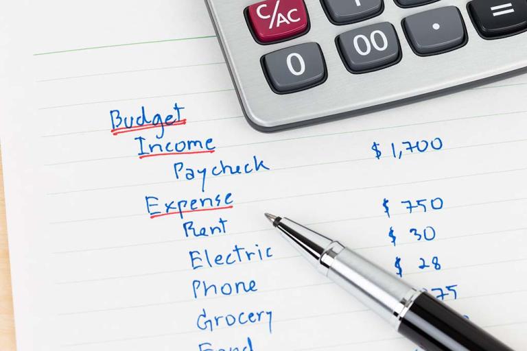 a calculator and pen sit next to a list of someone's expenses, including rent, utilities, and groceries