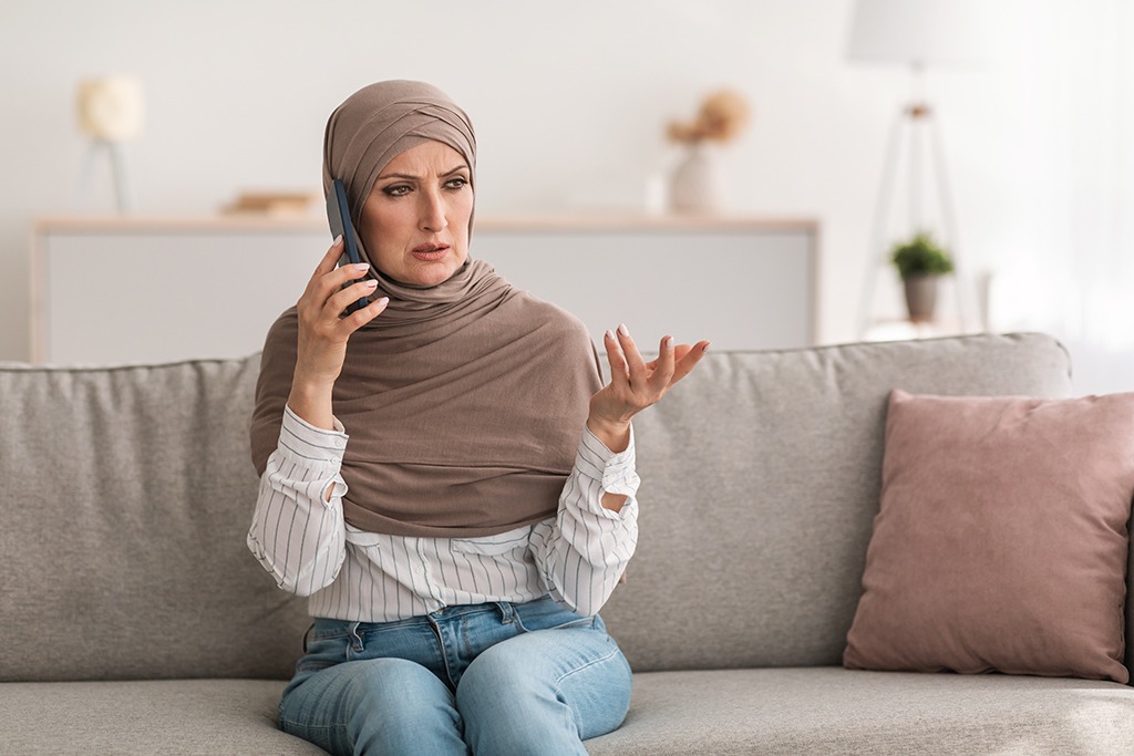 a woman in her 40s wearing an al amira talks on her cell phone, looking concerned