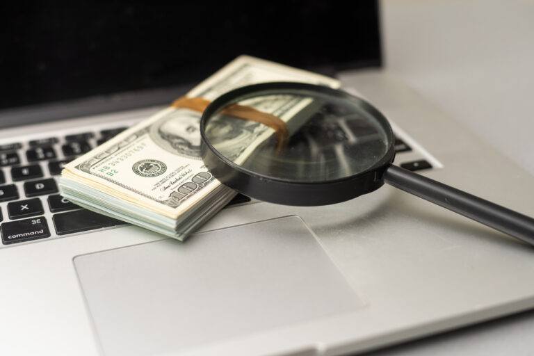 Magnifying glass and dollar bills on laptop.