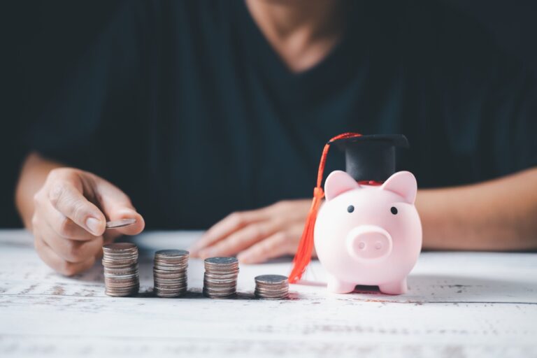 Man stacking coins next to piggy bank with graduation cap