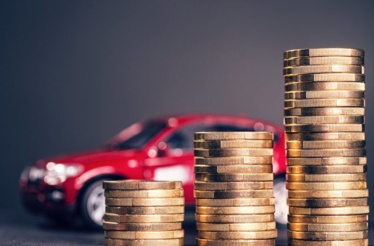 Rising stacks with coins and a red car in the background