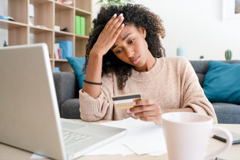 Young woman stressed by credit card debt sitting at table