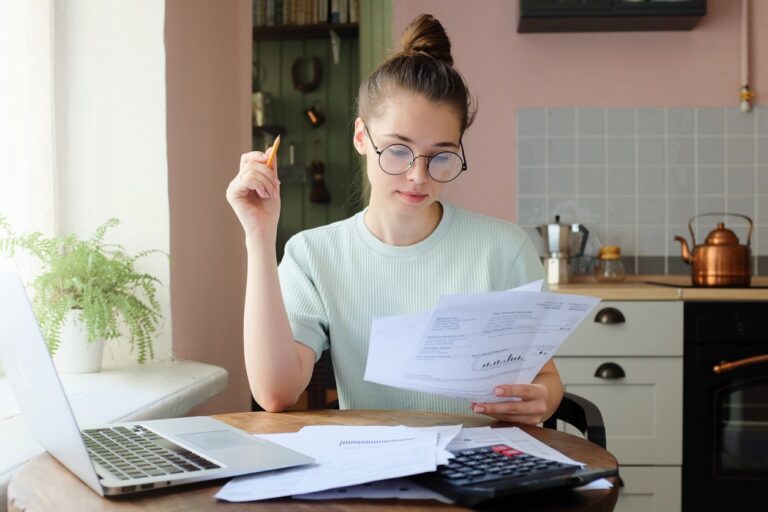 Image of woman at desk with laptop and calculator looking over paper of confirmed debts