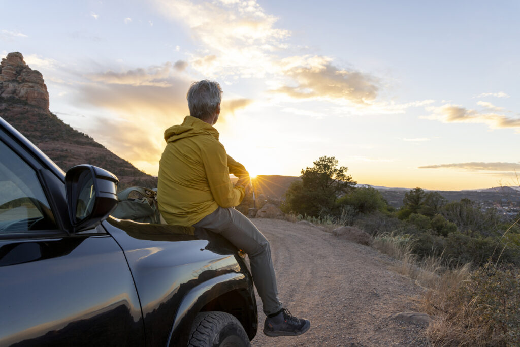 Man sitting on hood of car watching sunset - wondering about future