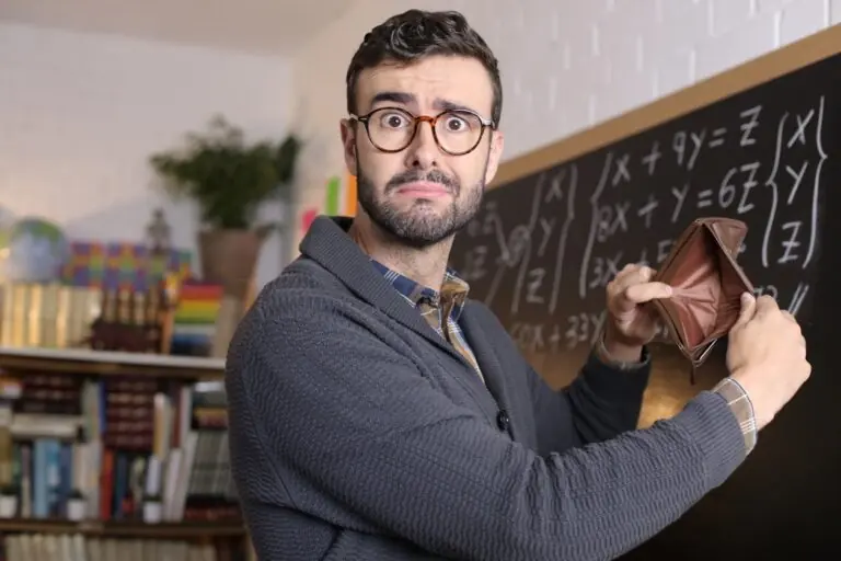 Teacher showing empty wallet in front of chalk board in classsroom