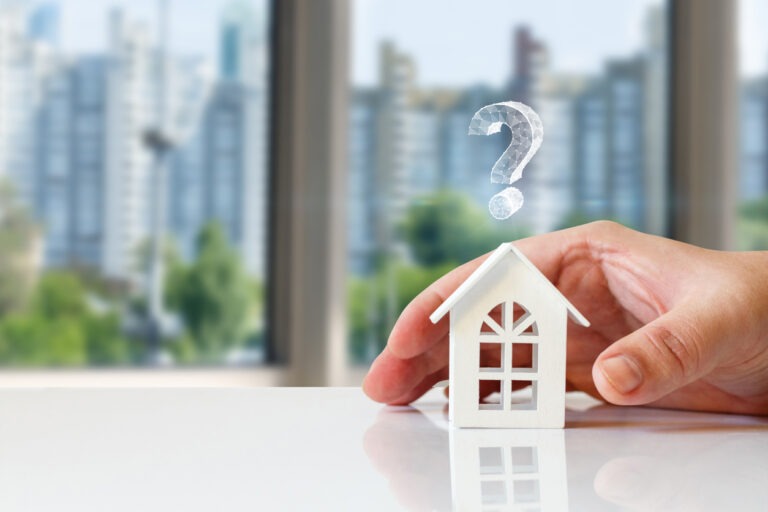 Hand with wooden house figurine and question mark above