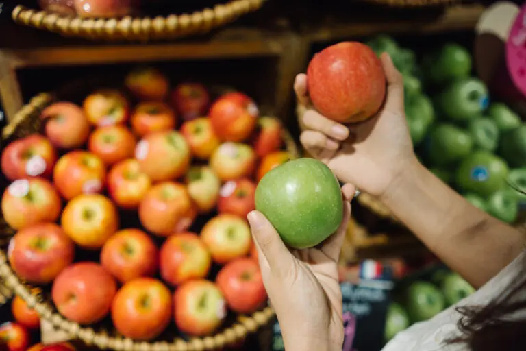 Woman comparing green apple to red apple in market