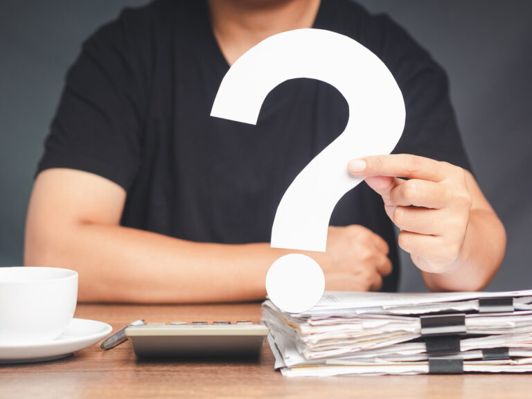 A young man in a black casual is holding a white question mark symbol while sitting at the table